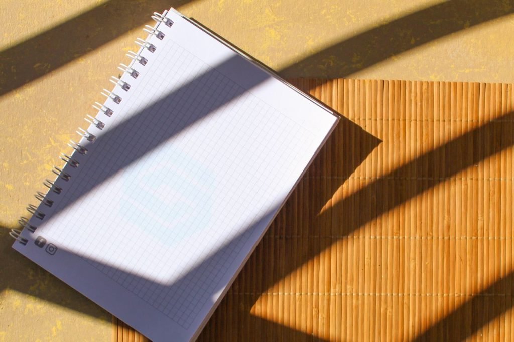 A spiral notebook placed on a bamboo mat with striking sunlight and shadow patterns.